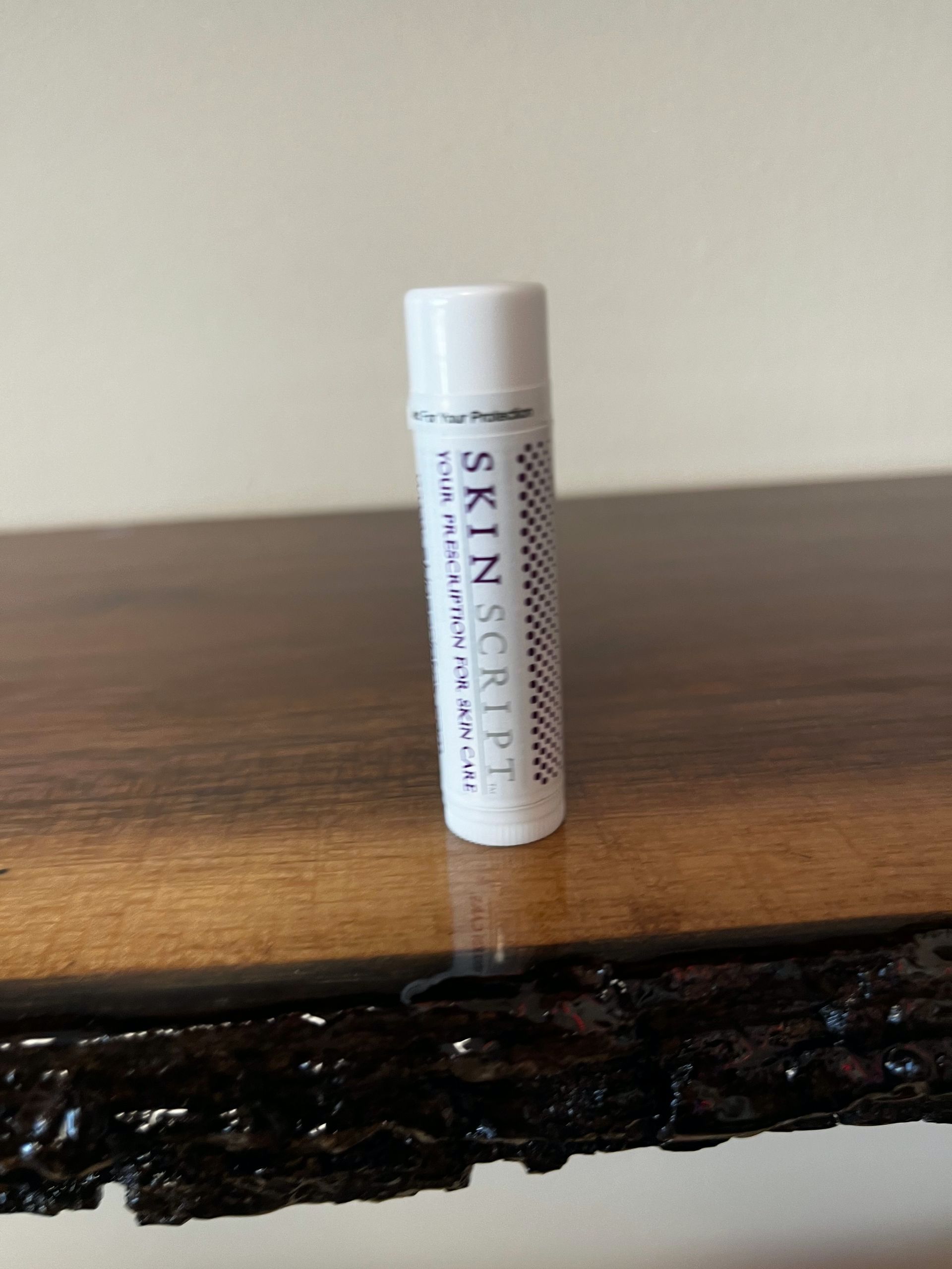 White tube of skin ointment standing on a wooden surface against a plain wall.