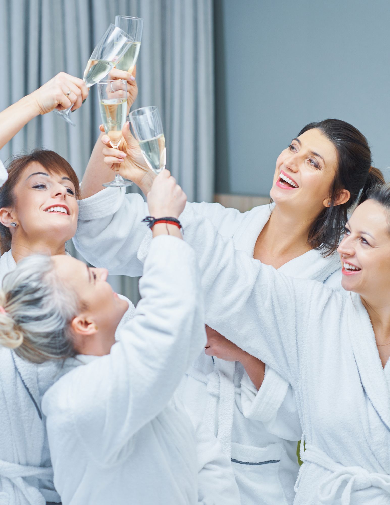 People in white robes toasting champagne glasses in a bright spa-like room