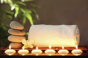 Spa setting with rolled white towel, stacked stones, candles, and a flower on a dark tray