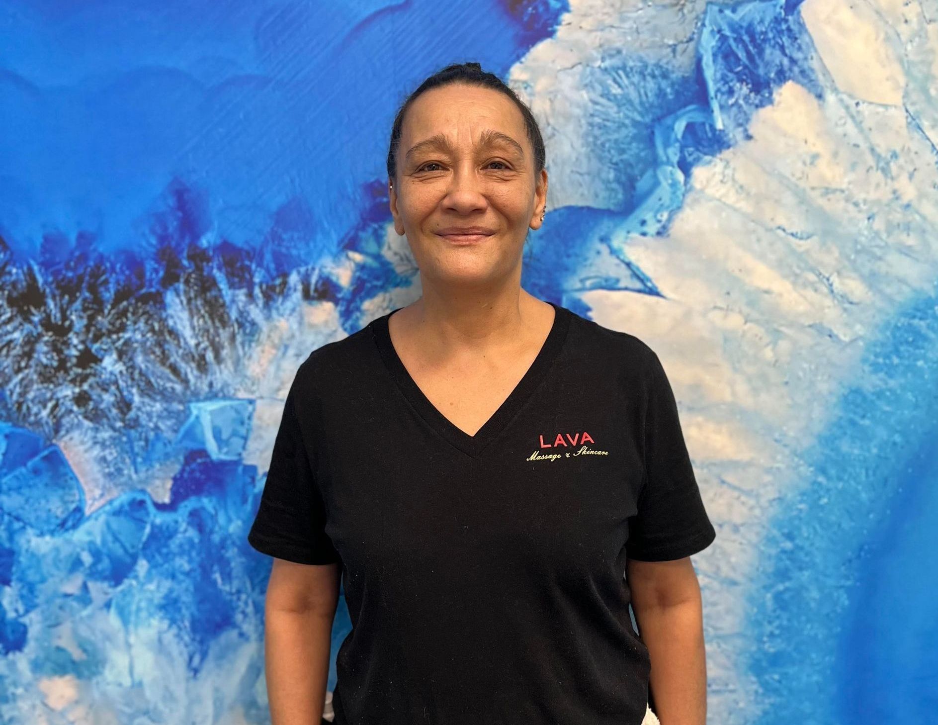 Person smiling in a black shirt standing before a blue abstract mural.