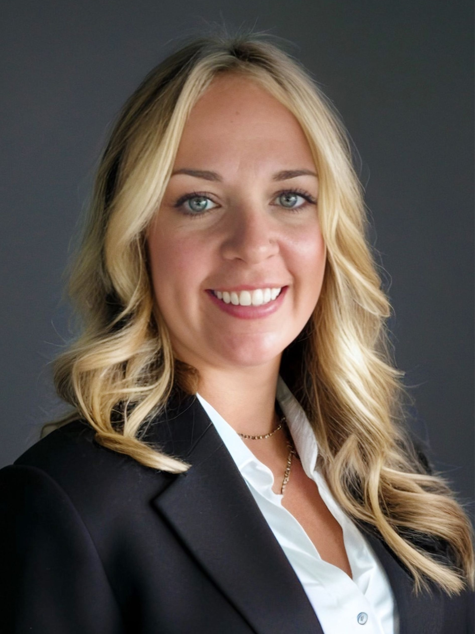 A woman in a black jacket and white shirt is smiling for the camera.
