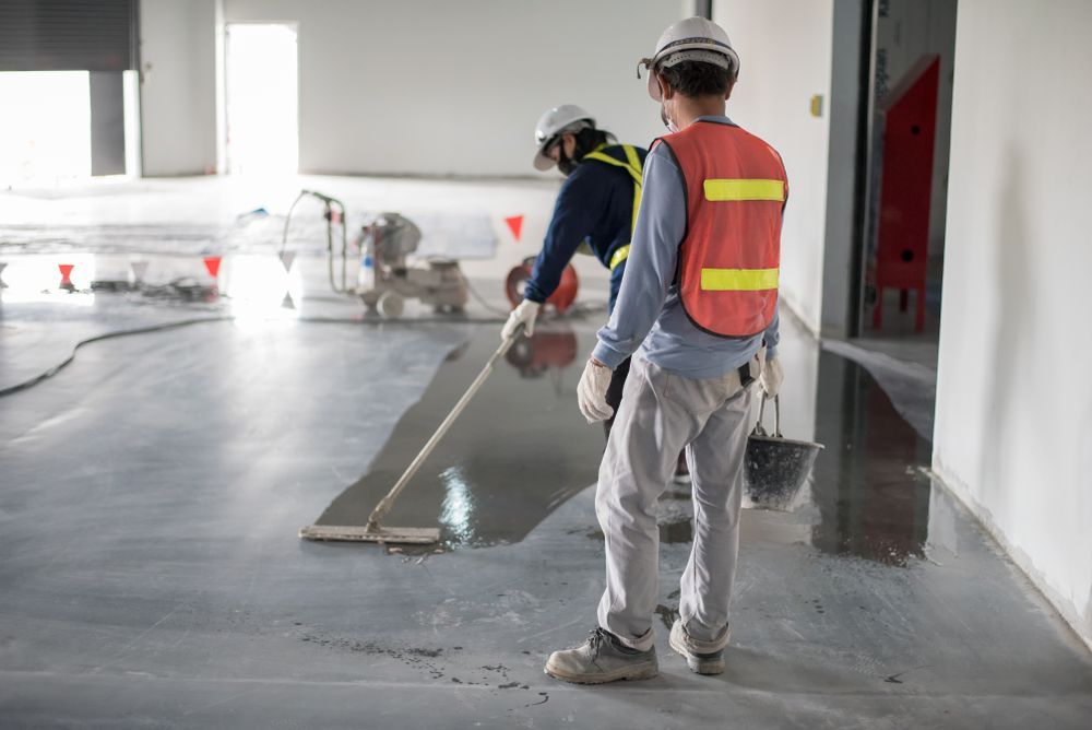 Two Construction Workers Applying A Grey Epoxy Coating To A Concrete Floor — Rocky Commercial Cleaners In Berserker, QLD