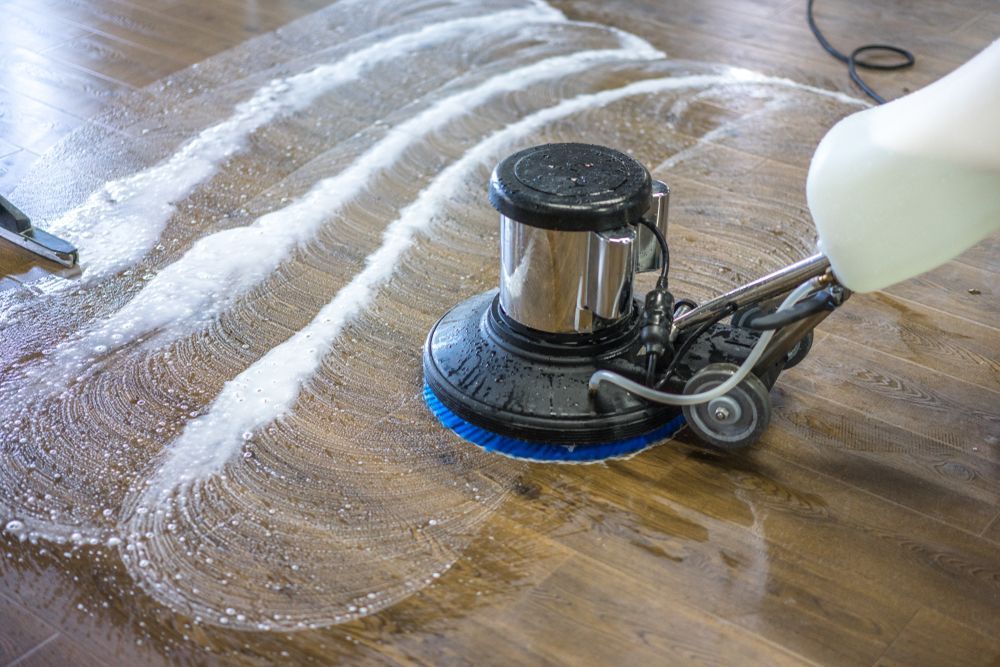 Floor Cleaning Machine Scrubbing A Wooden Floor With White Cleaning Solution — Rocky Commercial Cleaners In Berserker, QLD
