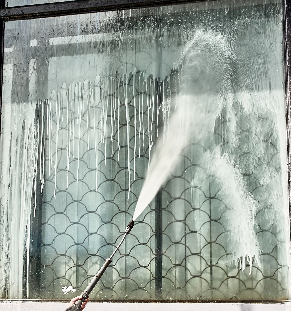 Person Using A Pressure Washer On A Window; Streaks Of Soap And Water — Rocky Commercial Cleaners In Berserker, QLD