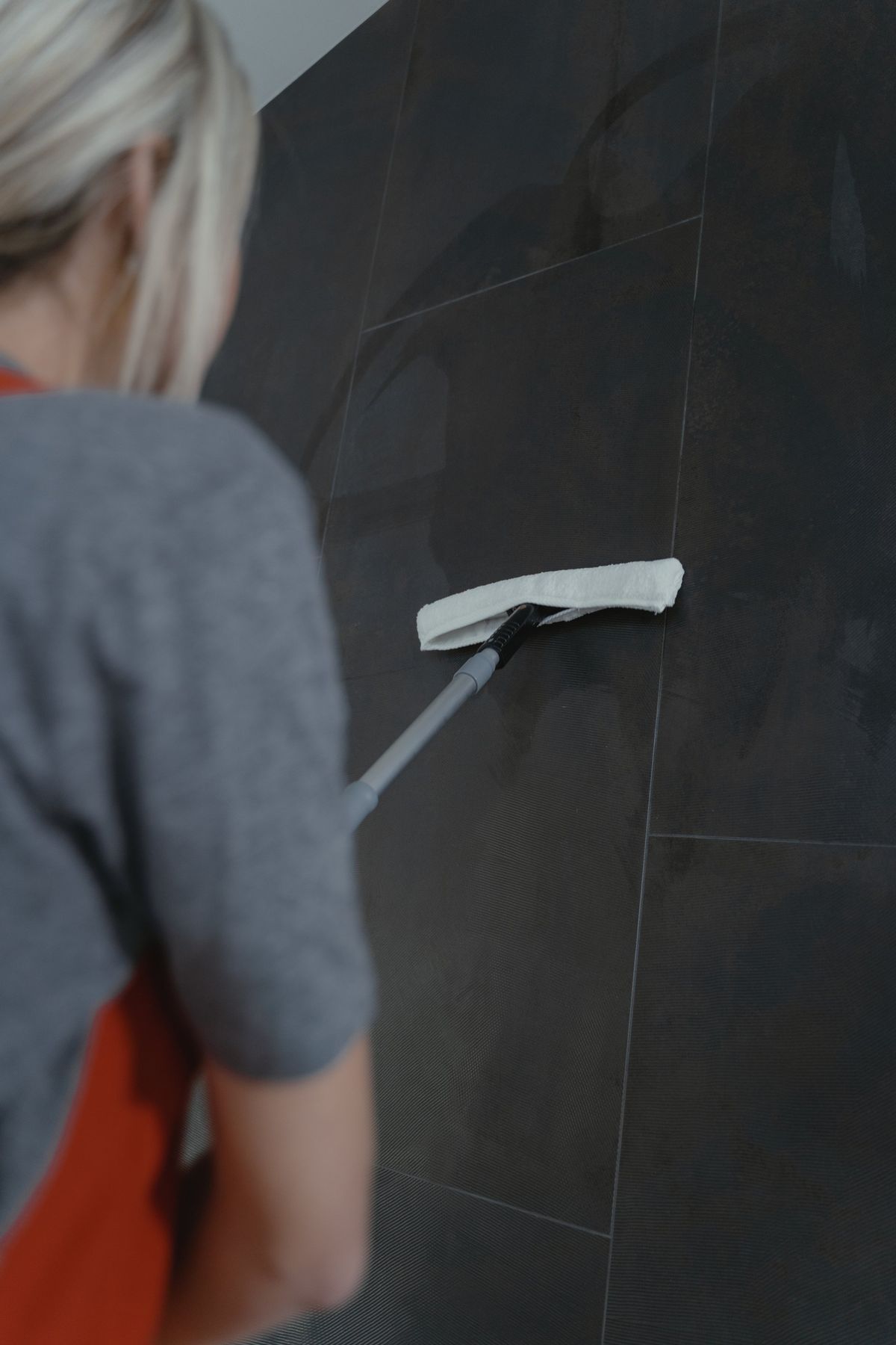 Woman Cleaning A Dark Tiled Wall With A Long-handled Squeegee  — Rocky Commercial Cleaners In Berserker, QLD