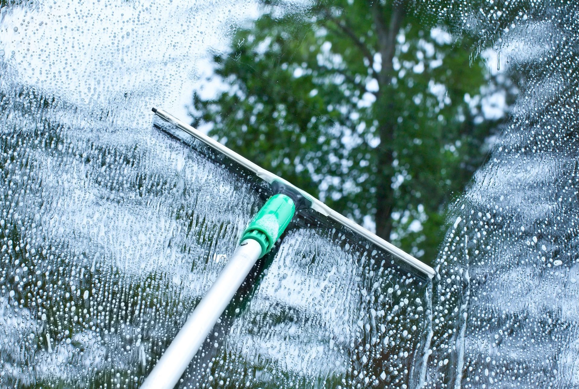 Squeegee Cleaning A Soapy Window; Trees Visible Through Glass — Rocky Commercial Cleaners In Berserker, QLD