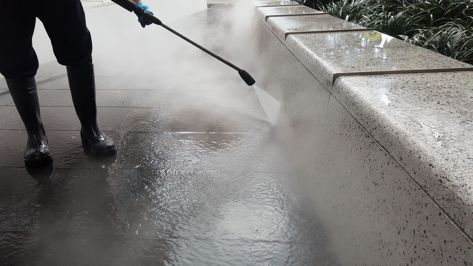 Person Power Washing A Stone Wall And Walkway; Water Sprays, Creating Mist — Rocky Commercial Cleaners In Berserker, QLD