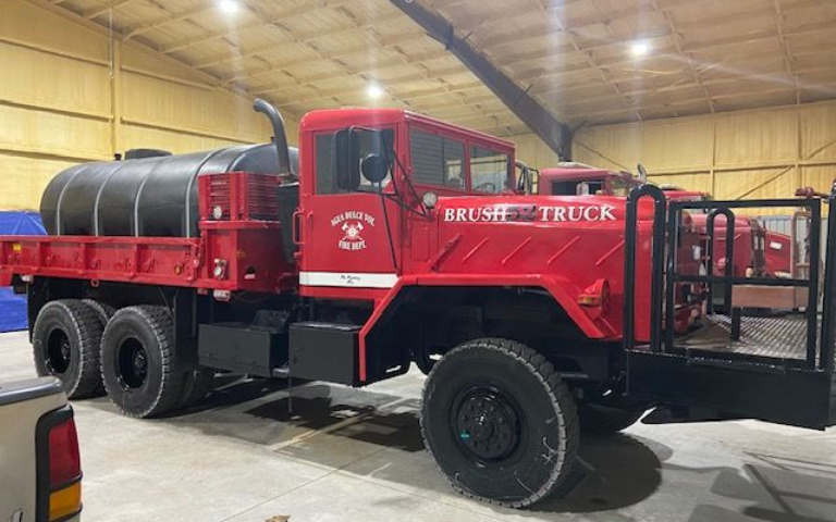 Red fire truck with tank, parked indoors in a warehouse-like garage