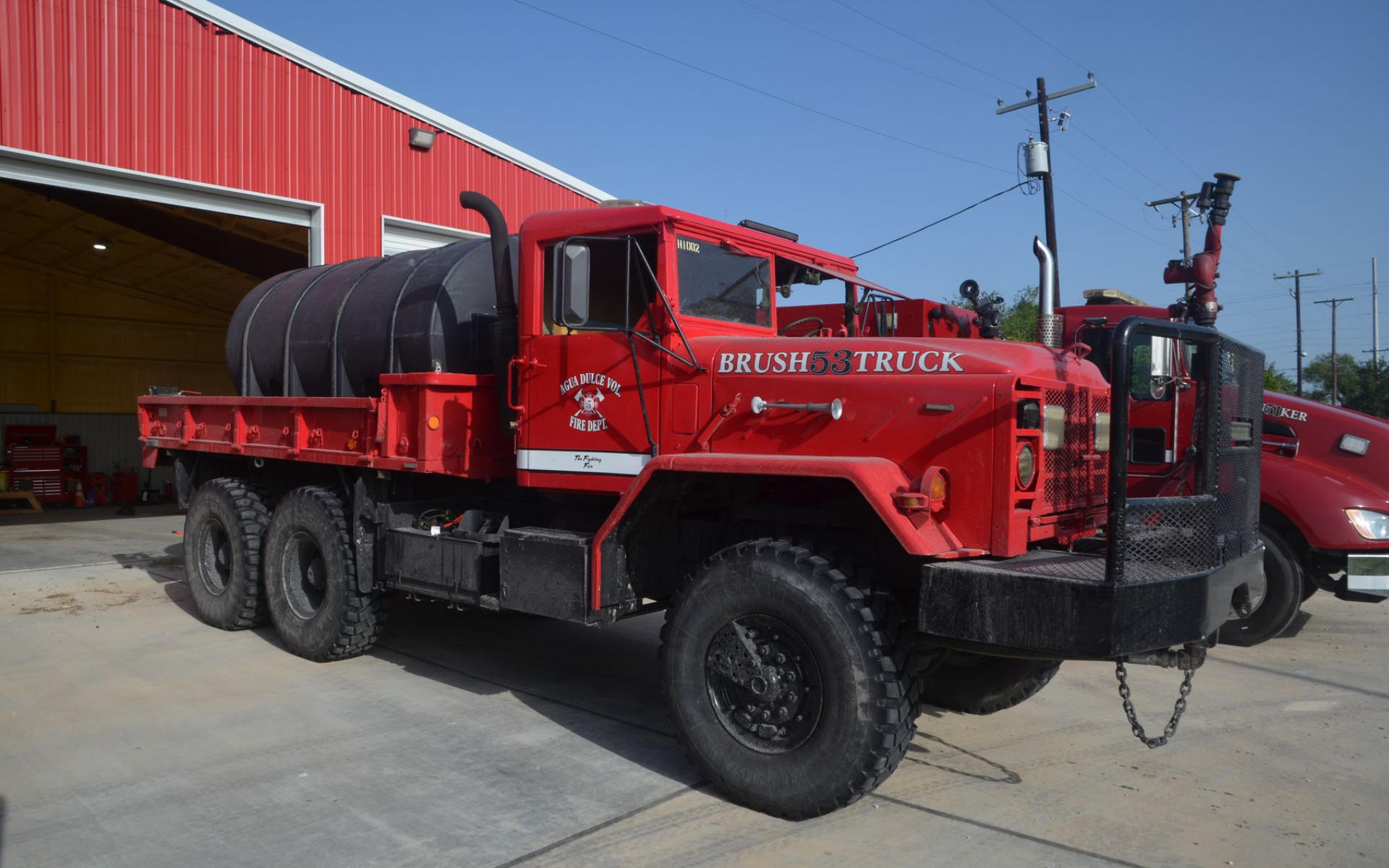 Red fire tanker truck parked beside a red building under a clear blue sky