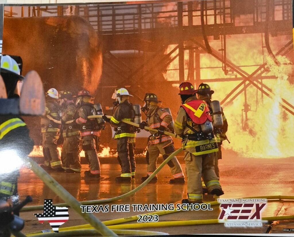 Firefighters in gear battling a large blaze at a training school, with flames and smoke filling the scene