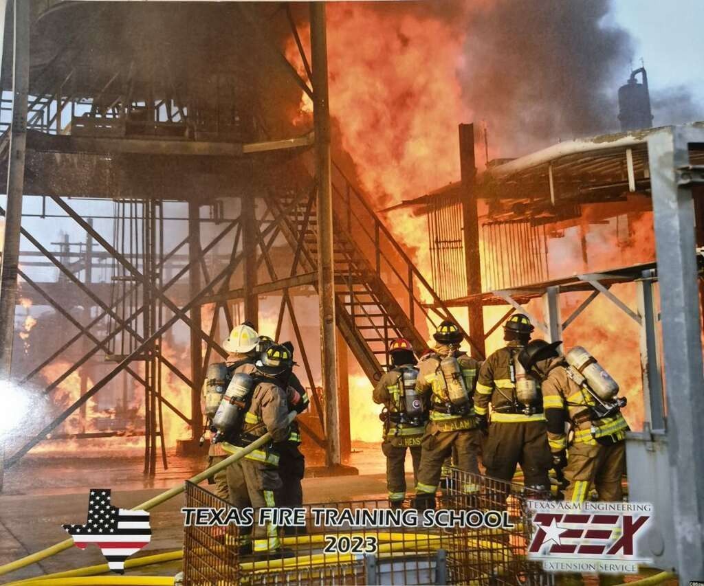 Firefighters in yellow gear battle a large blaze at an industrial structure, with thick smoke and flames.