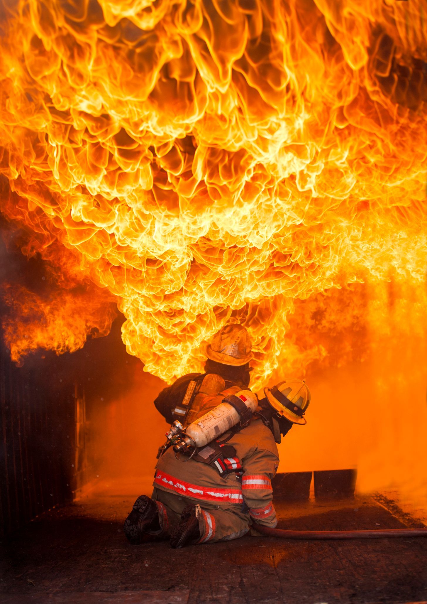 Firefighter crouching beneath a massive orange blaze in a dark room