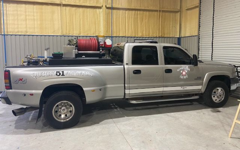 Silver pickup truck in a warehouse, side view, with a red hose reel mounted in the bed