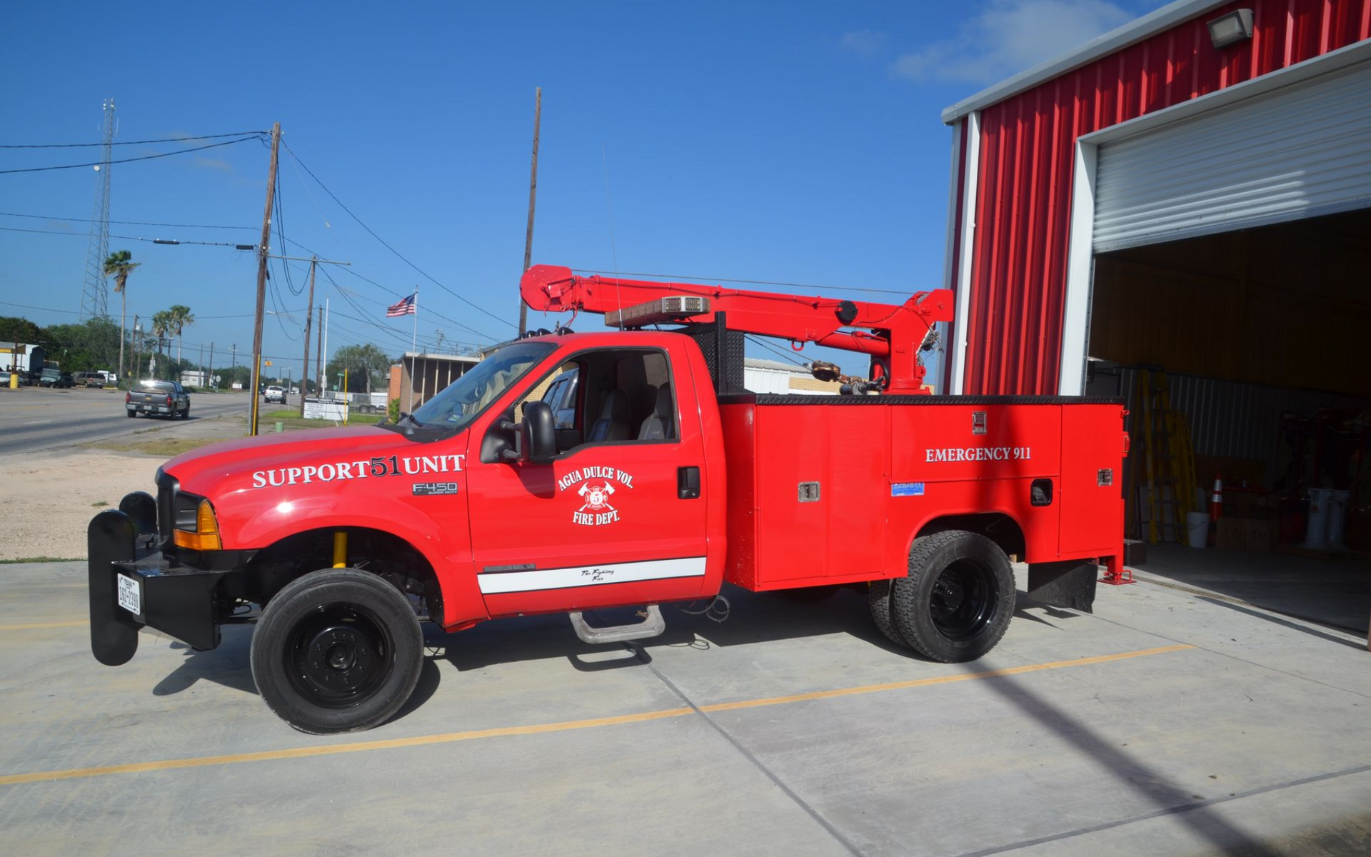 Red utility truck parked outside a garage, with a crane boom mounted on the bed.