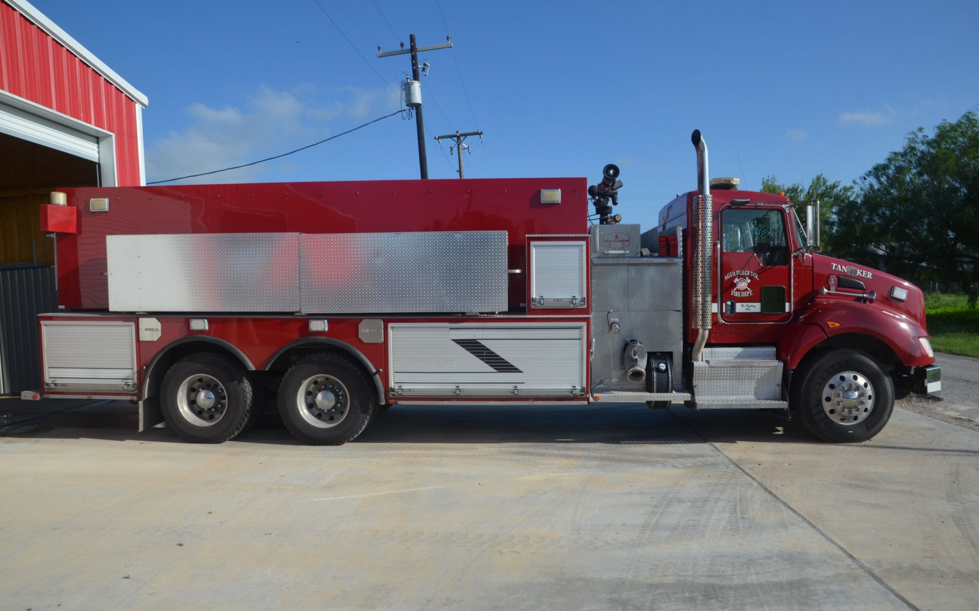 Red fire tanker truck parked beside a red building on a sunny day