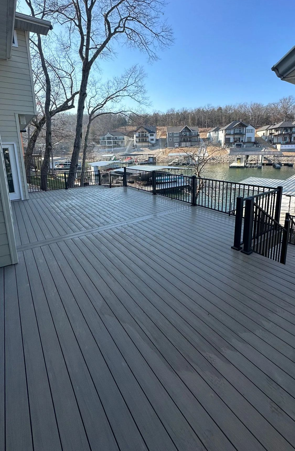 Wooden deck overlooking a snowy marina and hillside homes under a clear blue sky.