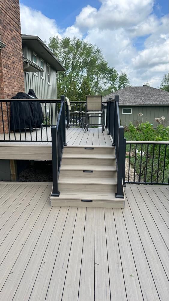 Back deck with beige stairs, black railings, and chairs overlooking a fenced yard