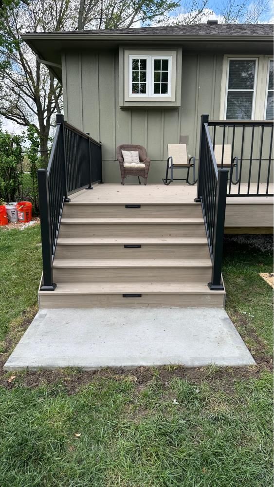Front porch stairs with black railings leading to a gray house entrance, with a small chair on the landing.