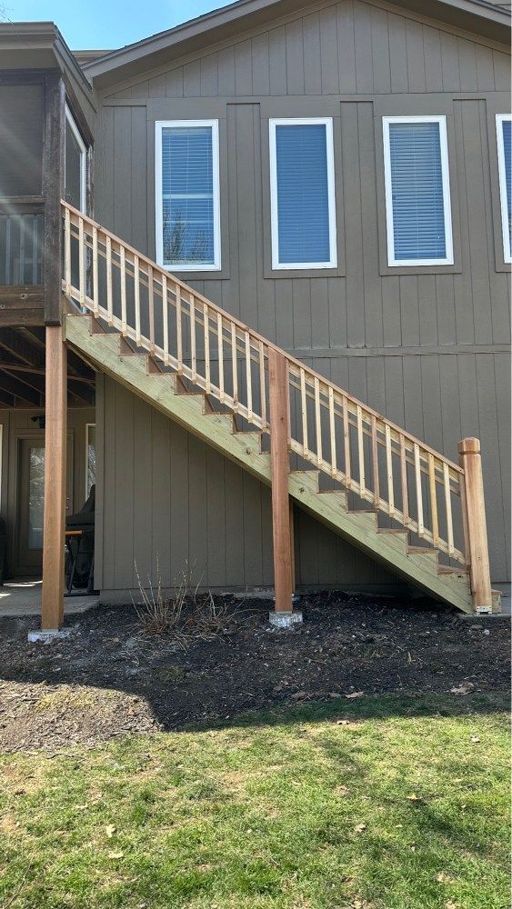Staircase and railings leading to an elevated brown house with three windows and a grassy yard