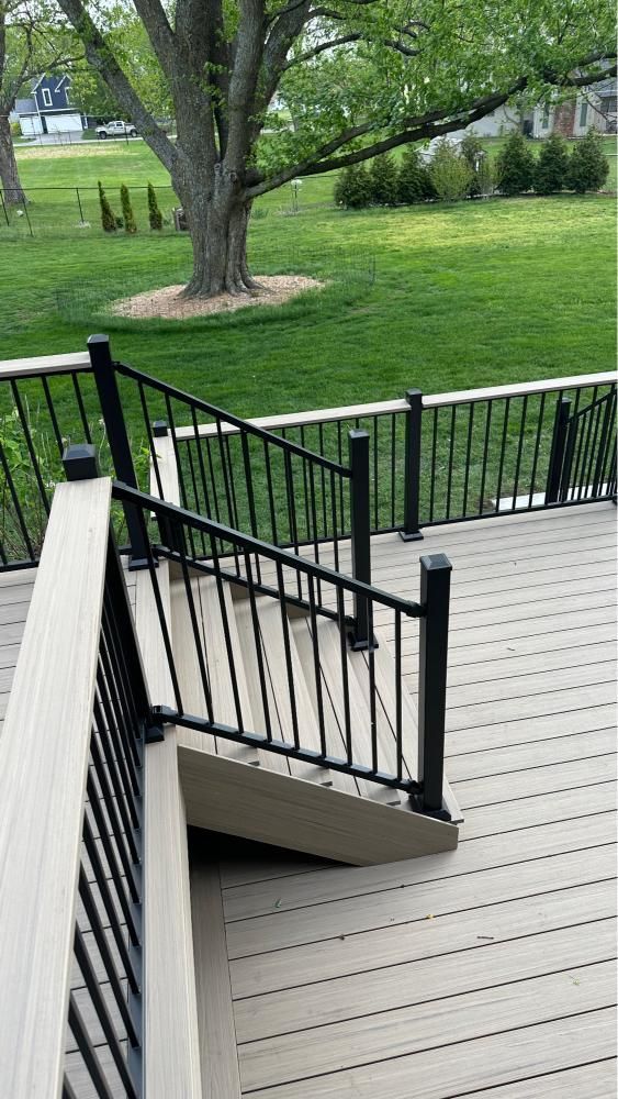Wooden deck stairs with black railings overlooking a green lawn and trees in a park-like yard