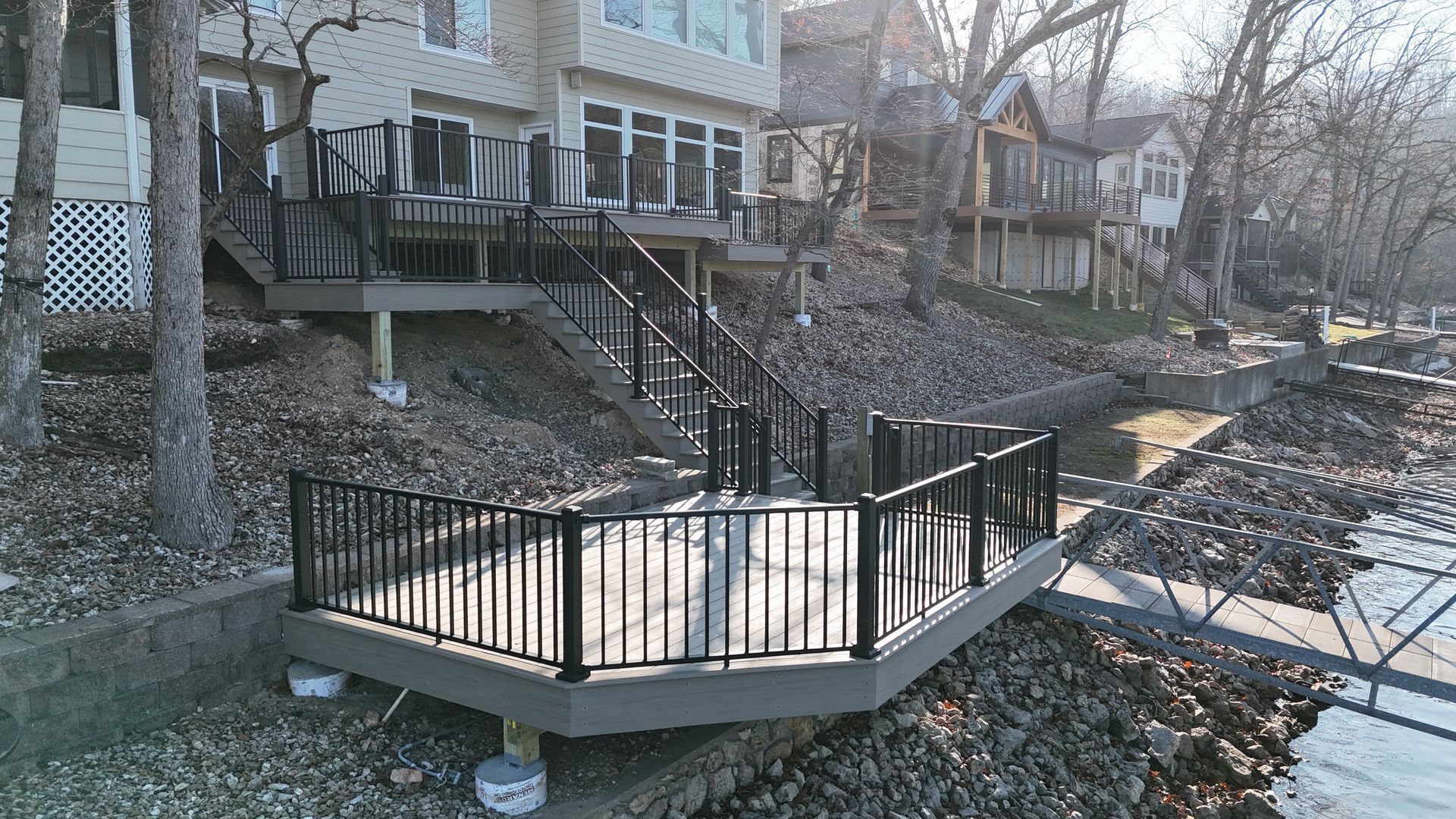 Small wooden footbridge over a creek beside houses and leafless trees in winter.