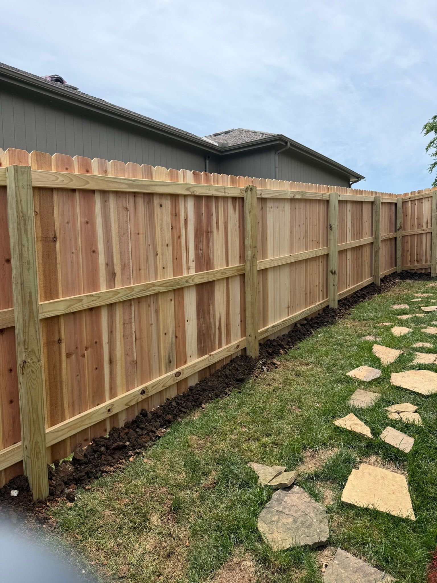 A wooden fence surrounds a lush green yard in front of a house.