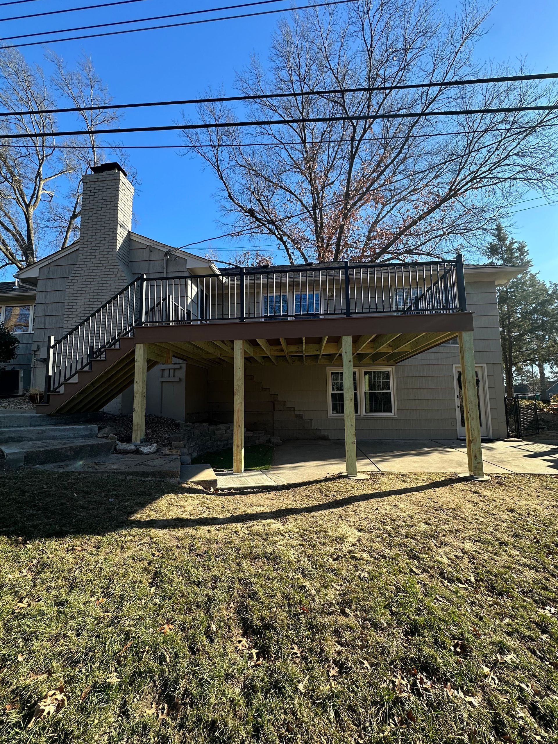 Exterior of a raised house with wooden deck, stairs, and support posts in a leaf-covered yard