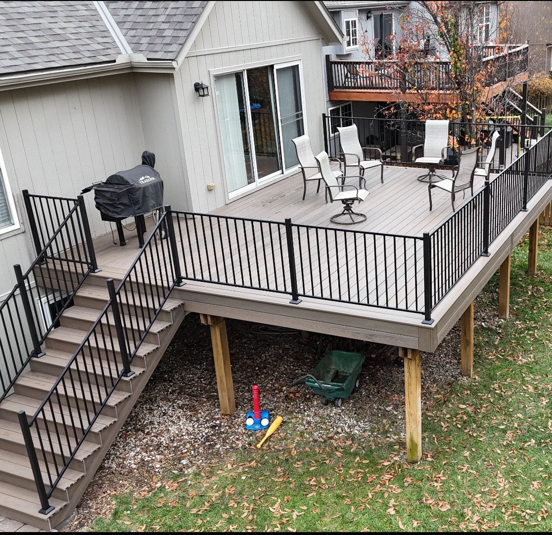 Back deck with black railing, patio furniture, grill, and stairs leading to a grassy yard below.