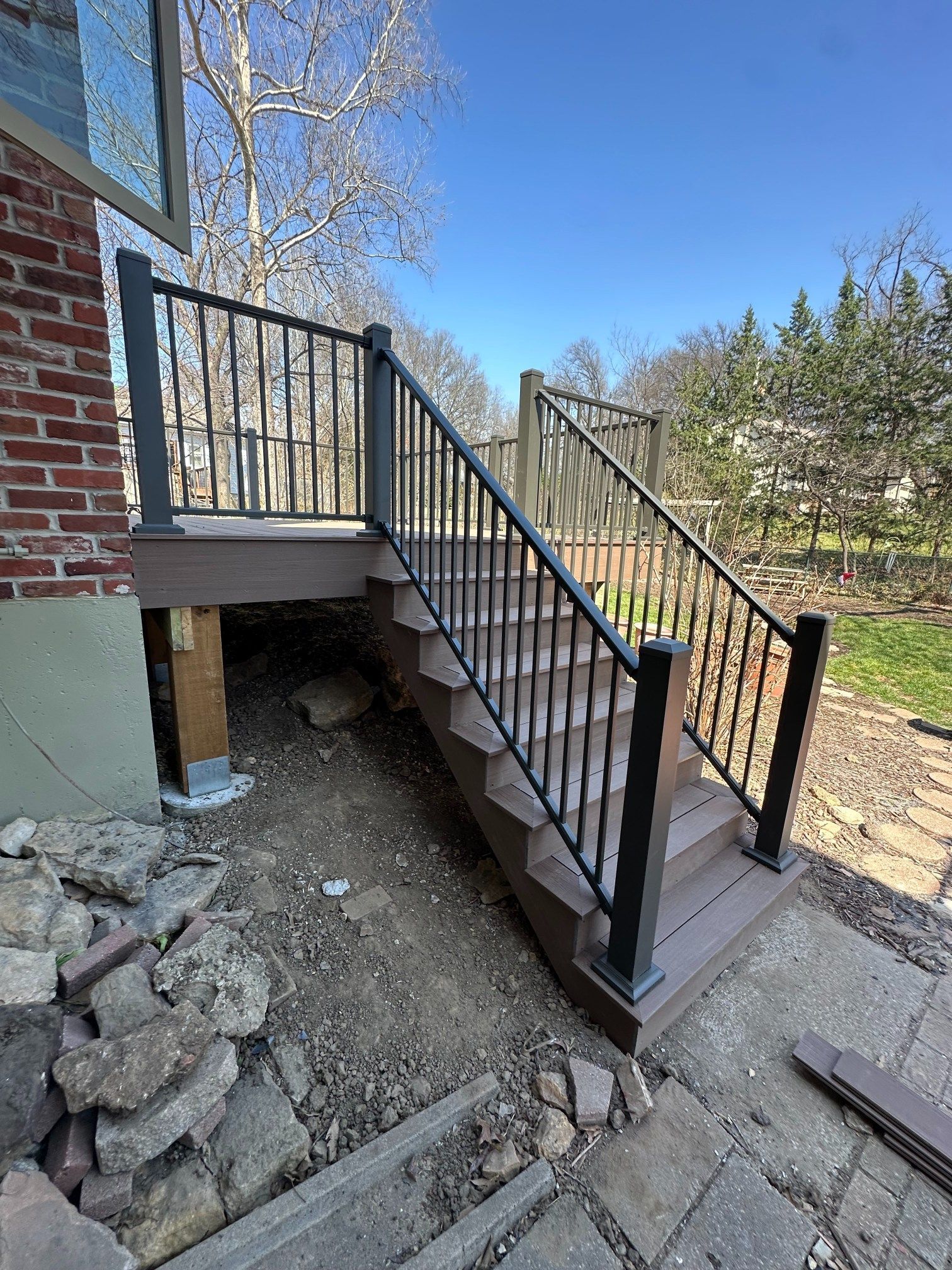 Black metal exterior staircase beside a brick house on a sloped yard, with concrete steps and railing.