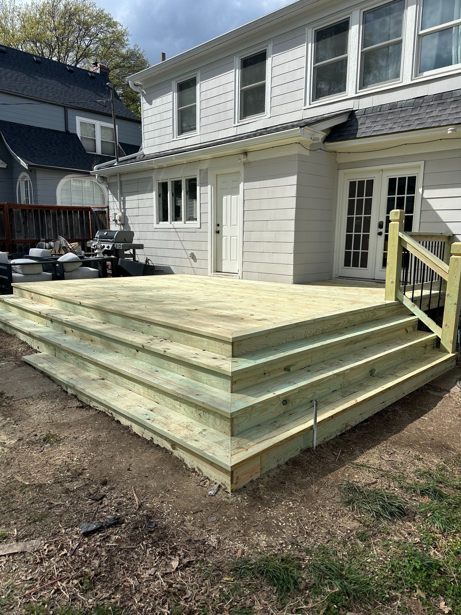 Backyard deck under construction beside a white two-story house with new steps and railings