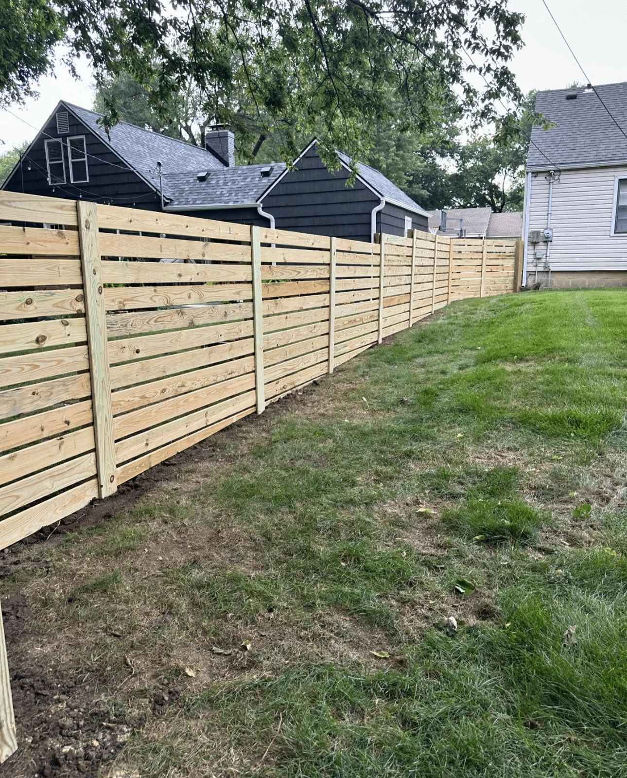 A wooden fence surrounds a lush green yard in front of a house.