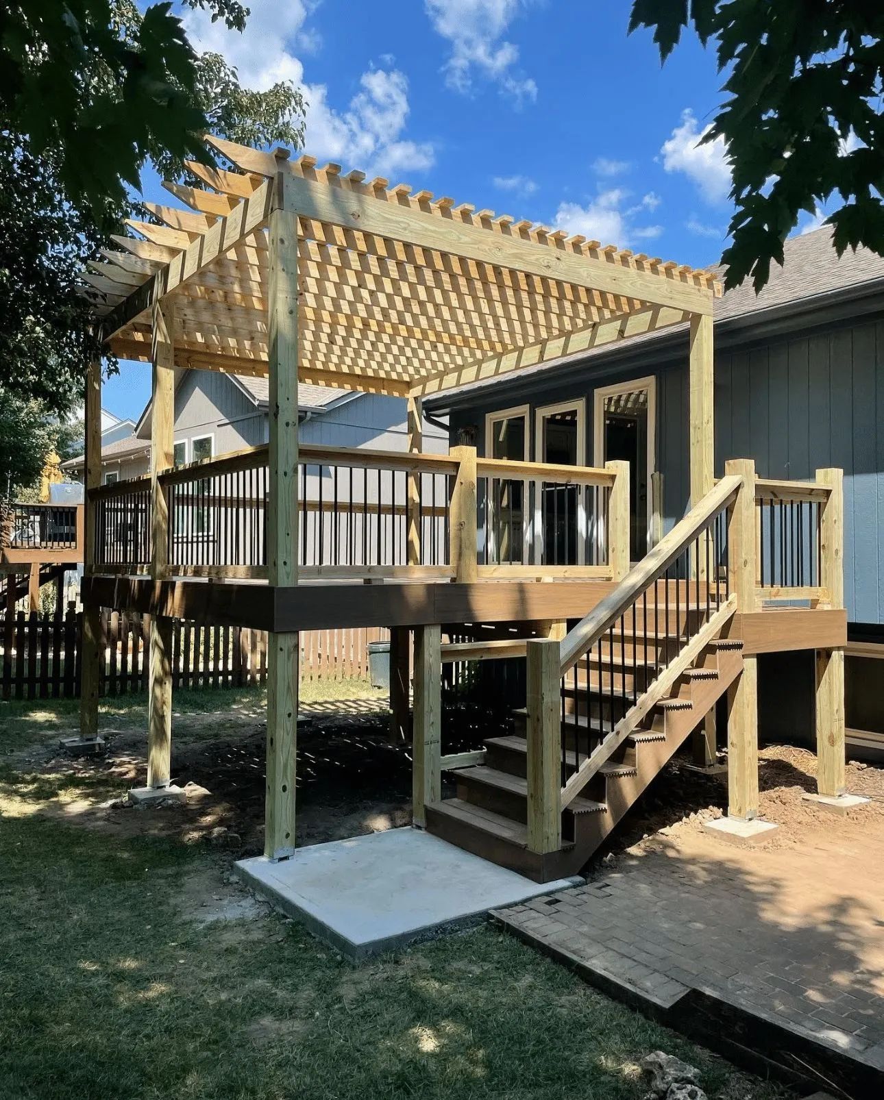 Wooden deck with pergola, stairs, and a concrete pad in a backyard.