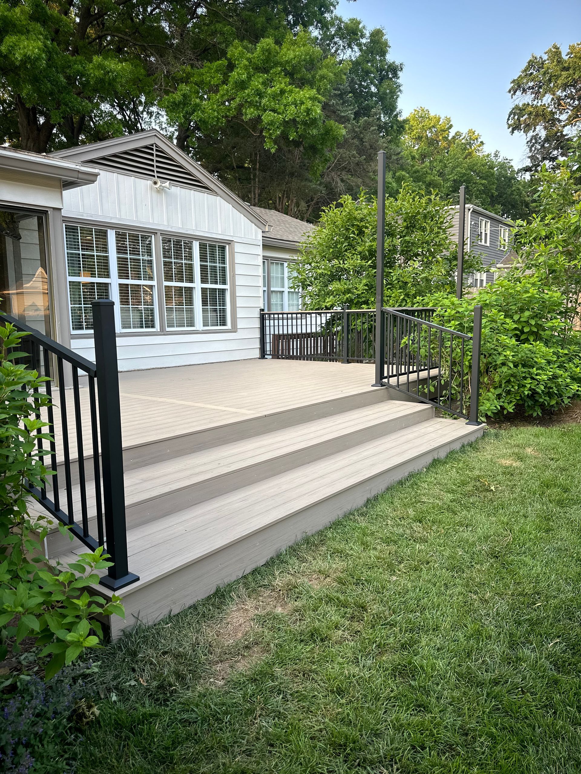 White house deck with stairs, black railings, and patio doors beside a grassy yard.