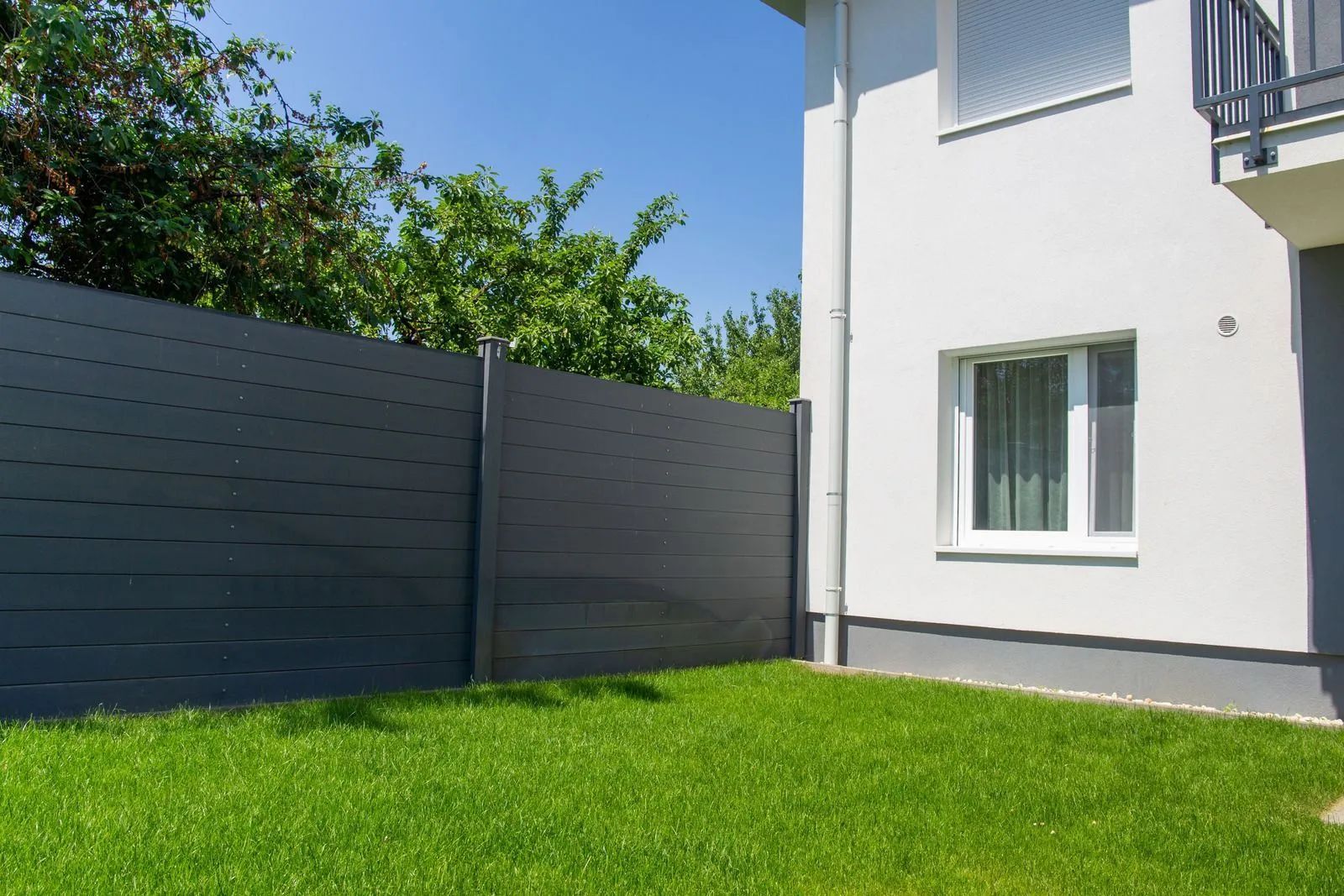 White house with gray fence and bright green lawn under a blue sky