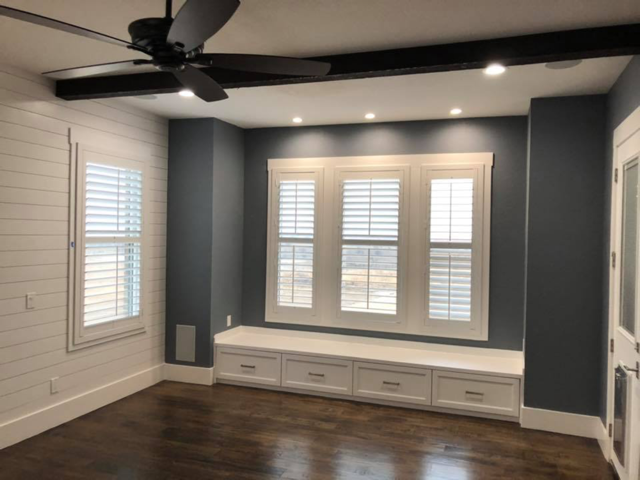 Room with dark wood floor, blue-gray walls, white window shutters, and a built-in bench with drawers.