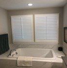 Bathroom with white shutters over a bathtub. A towel rests on the tub's edge.