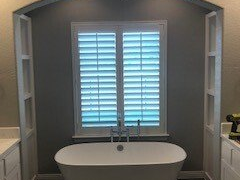 Bathroom with a white soaking tub, white shutters, and gray walls.