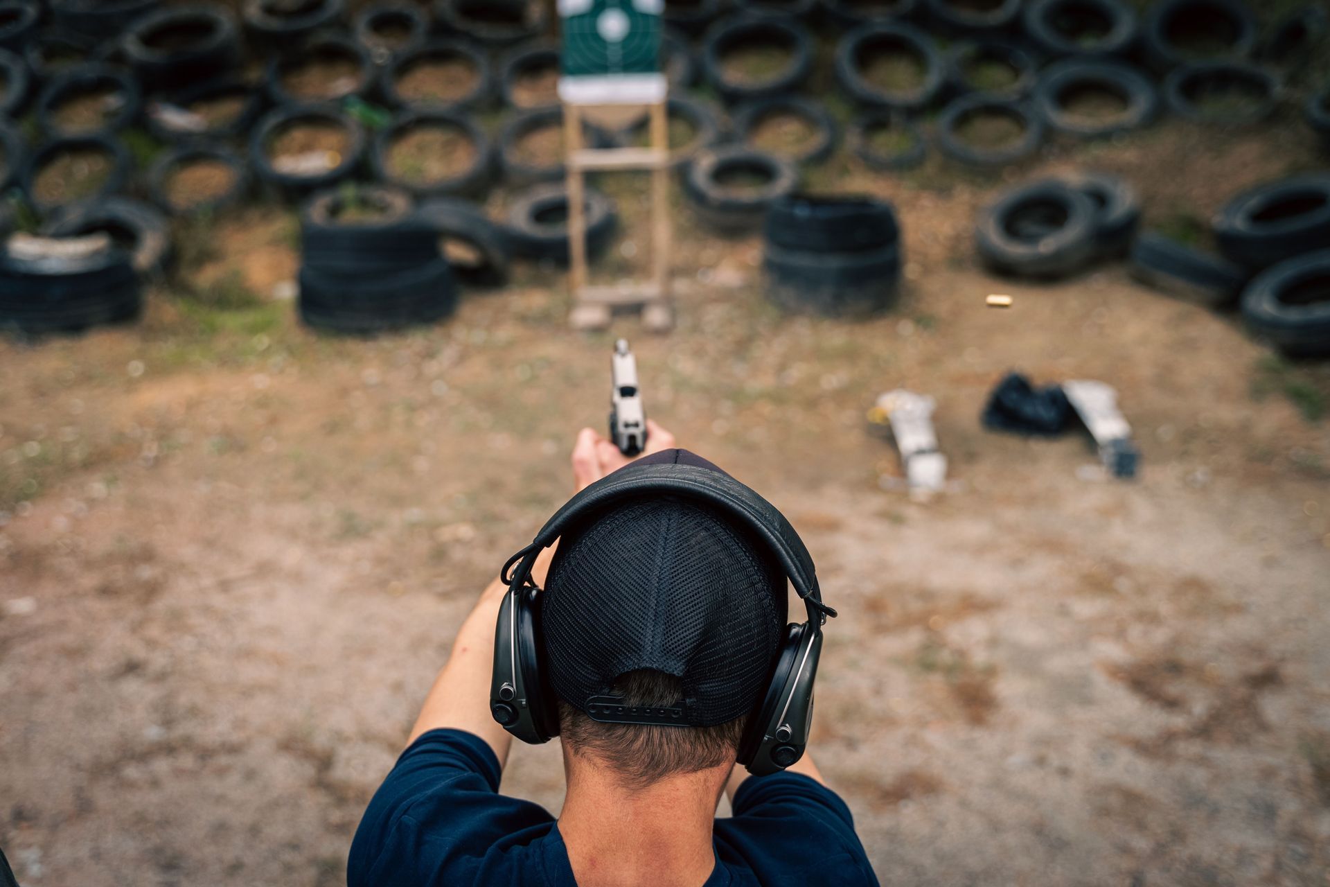 Person aiming a tactical rifle indoors, wearing safety glasses and headphones.