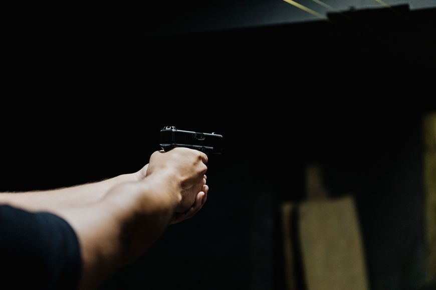Arm extended, aiming a handgun in a dimly lit indoor range