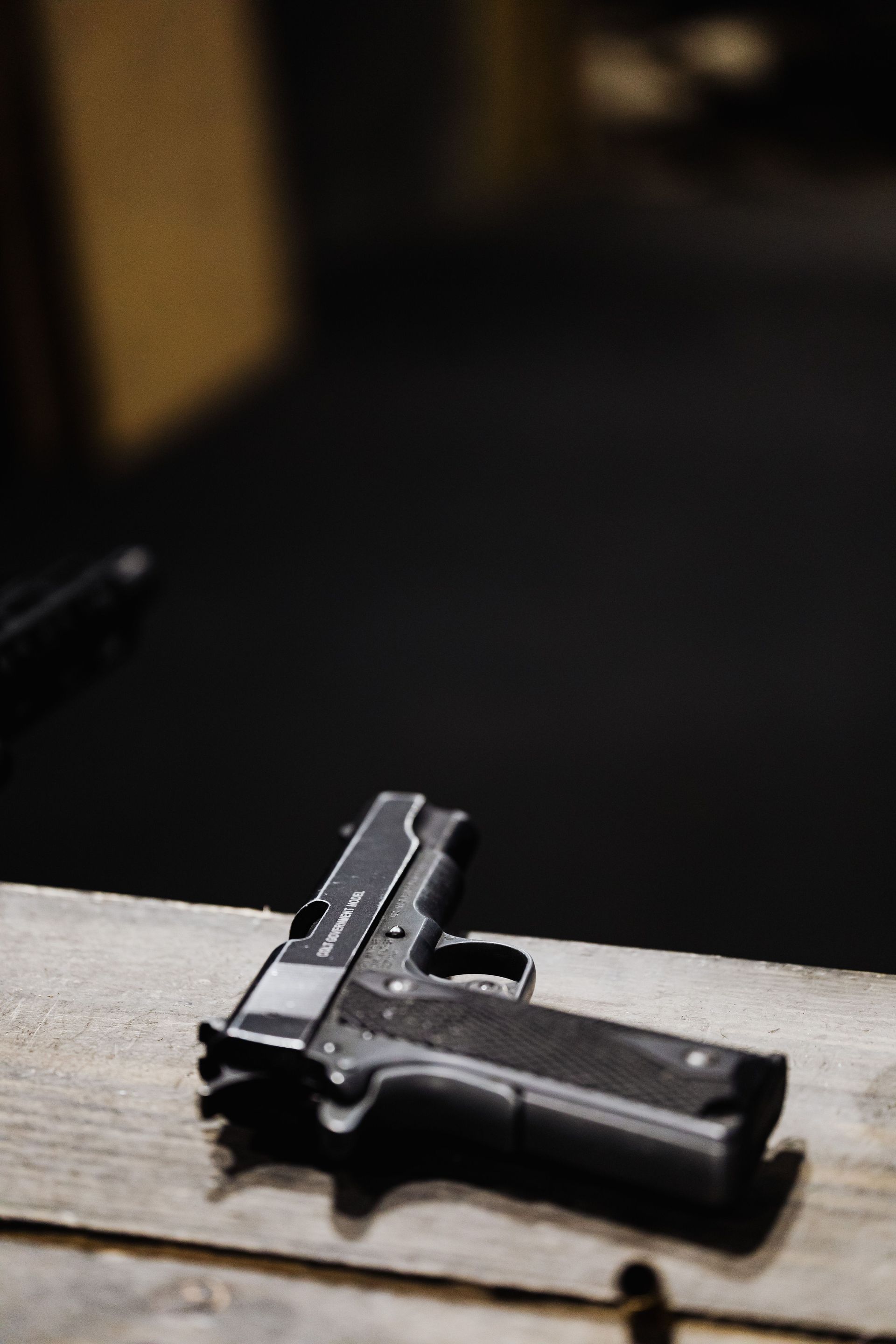 Person aiming a tactical rifle indoors, wearing safety glasses and headphones.