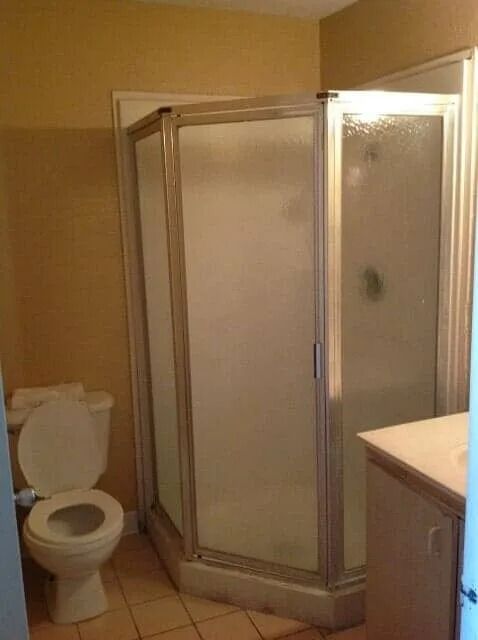Small bathroom with toilet, corner shower stall, and beige walls.