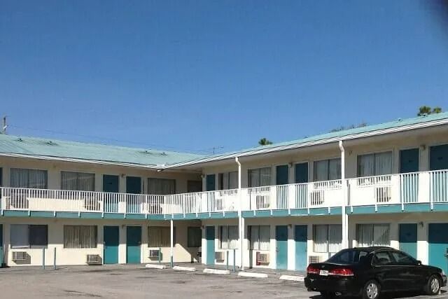 Two-story motel with turquoise doors and white railings under a clear blue sky; black car parked outside