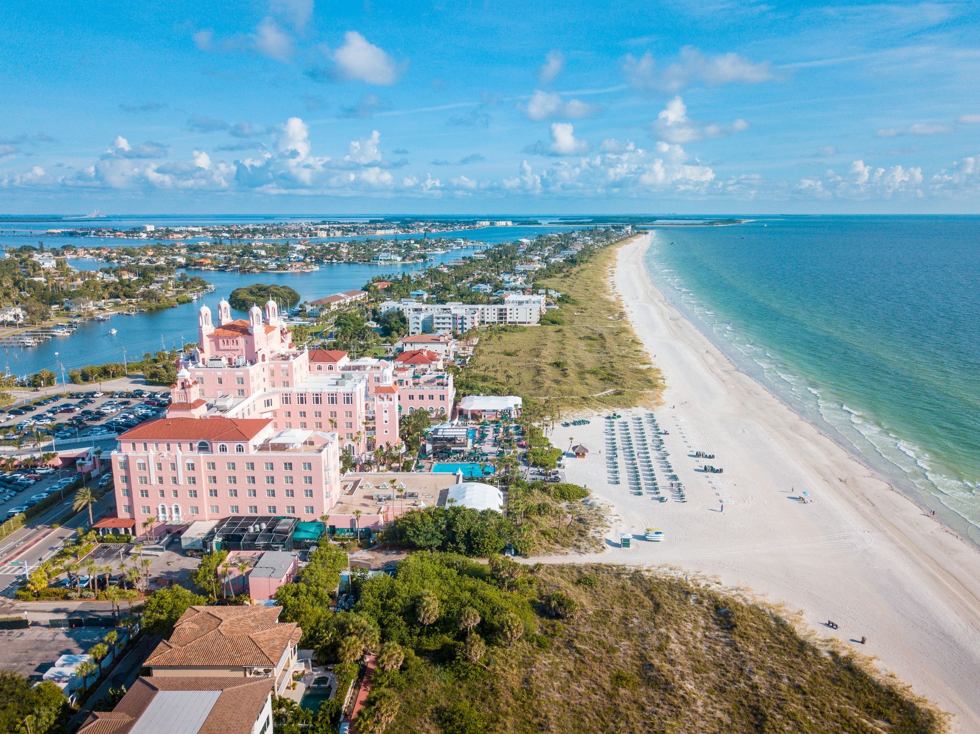 Aerial view of a pink beachfront resort beside a white sandy shore and turquoise ocean under a blue sky