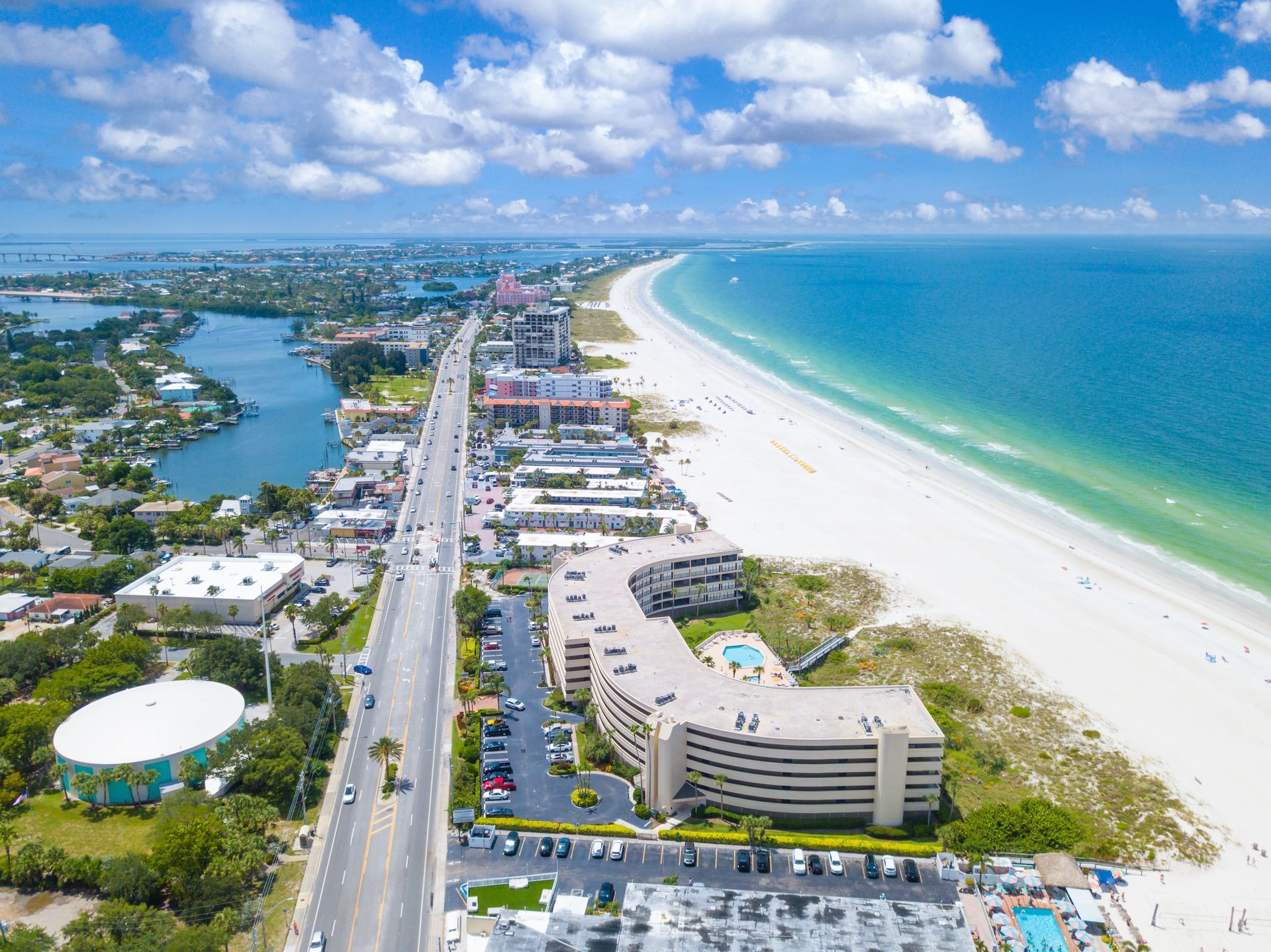 Aerial view of a coastal road beside white sand beach and turquoise ocean under a blue sky