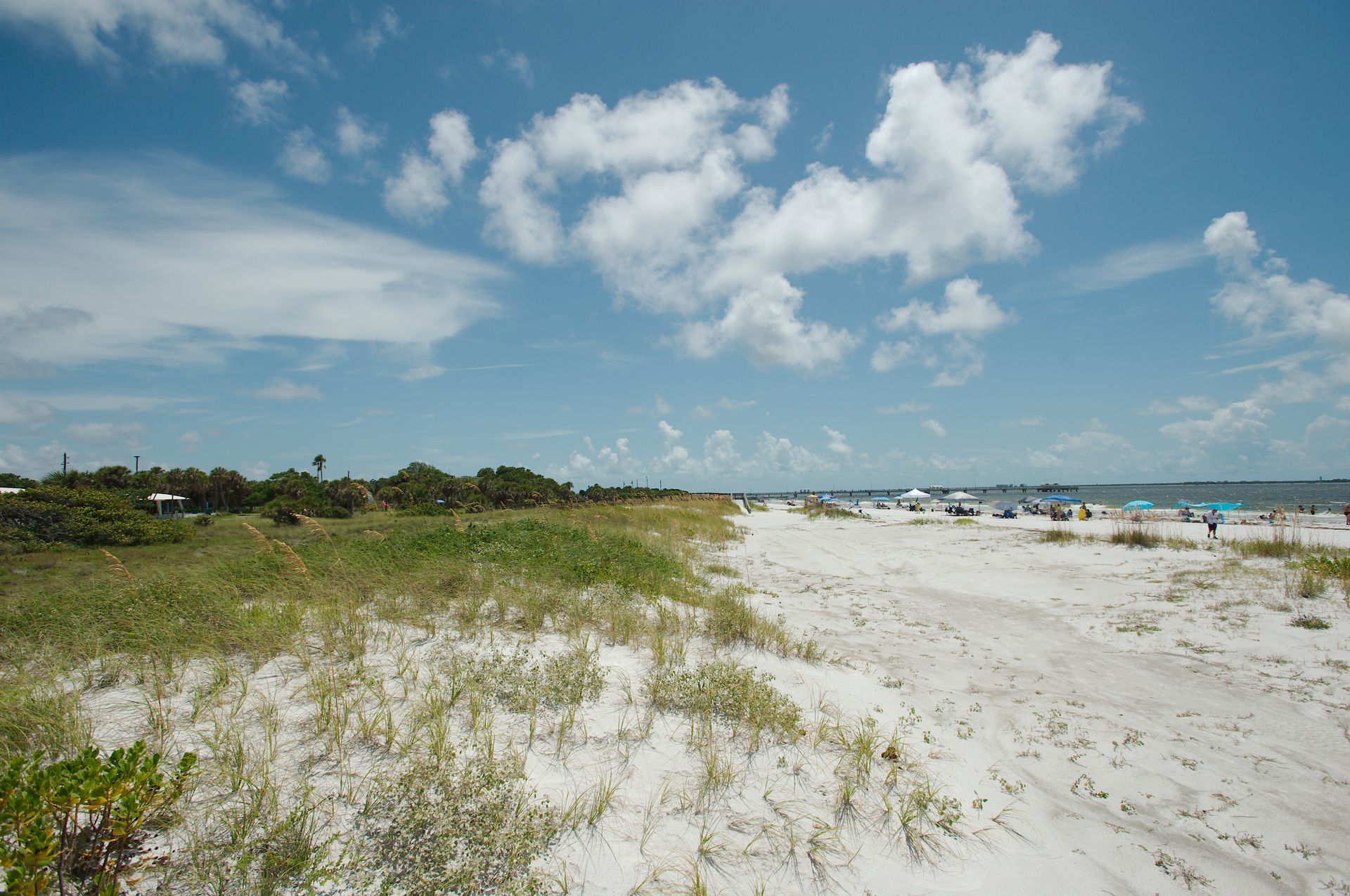 Sunny beach with white sand, dune grass, and blue sky with scattered clouds