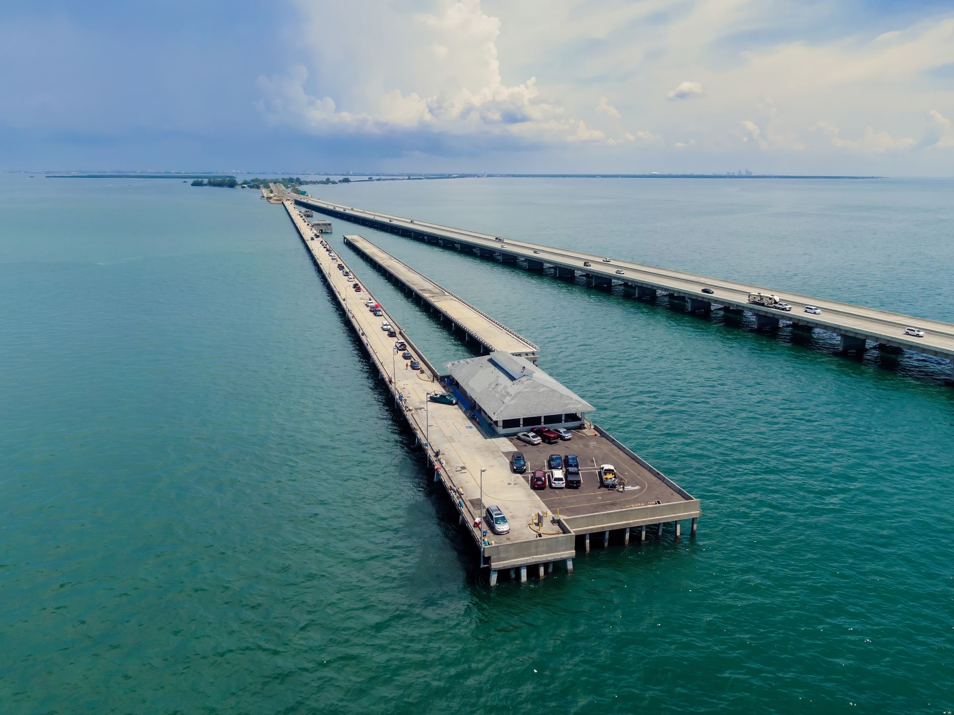 Aerial view of a long pier stretching into turquoise water under a cloudy sky