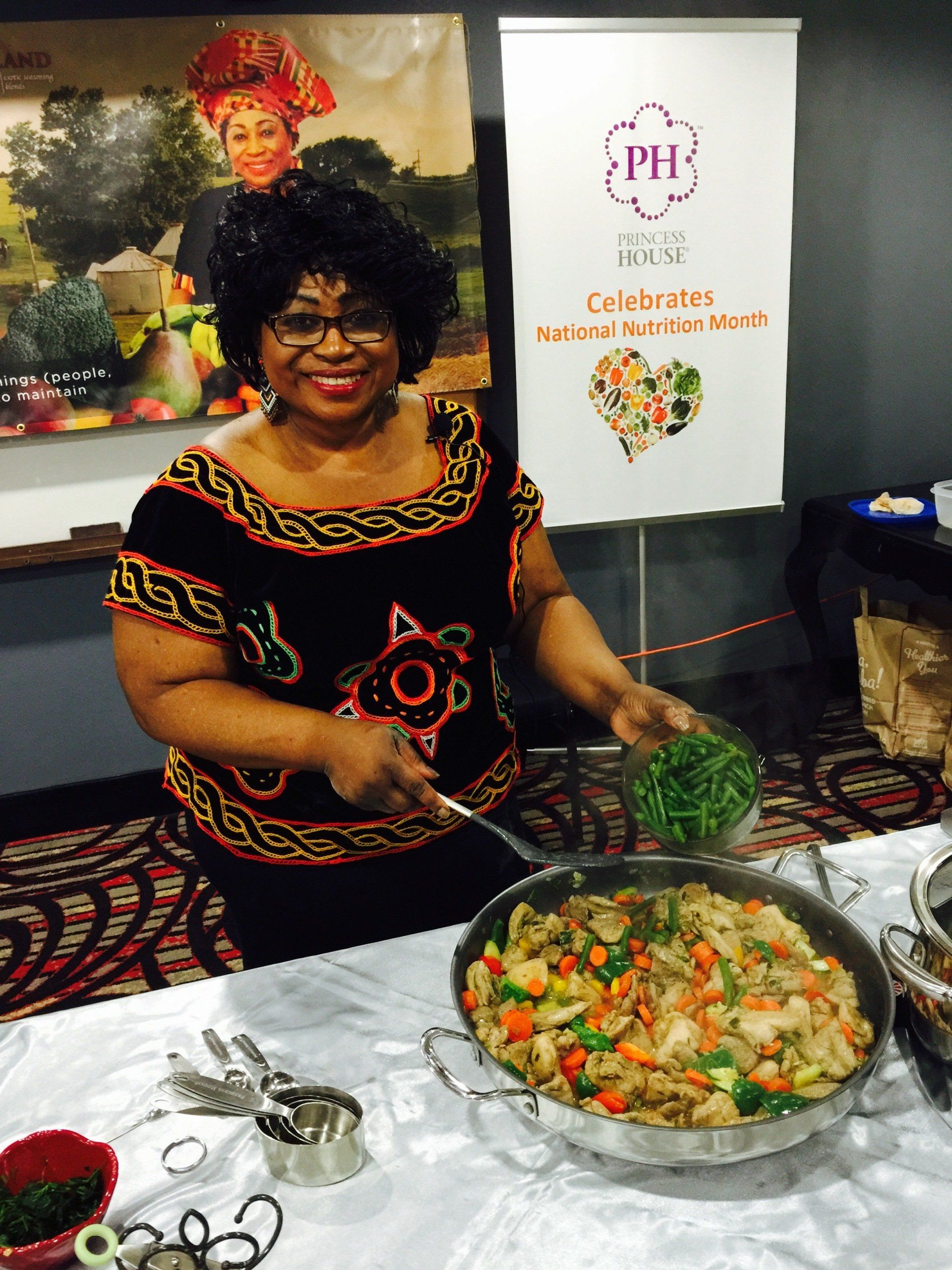 Woman adding peas to stir-fry in a large pan at a food demonstration booth.