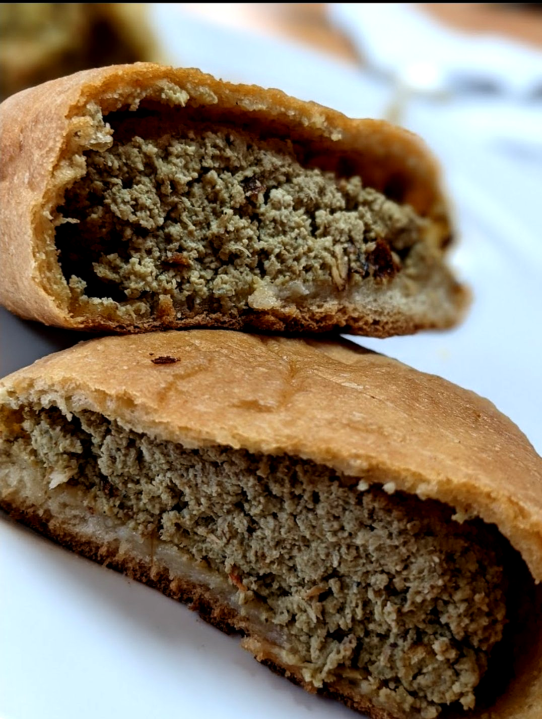 Two halves of a baked pastry filled with a gray-green, textured meat filling, on a white plate.