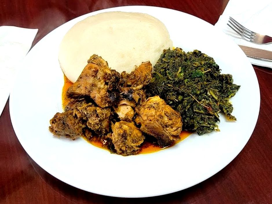 Plate with chicken, greens, and a large ball of white food, on a table.
