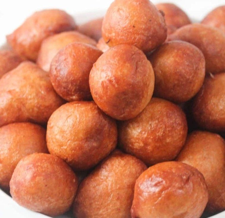 Golden-brown puff puffs piled high in a white bowl, a popular Nigerian fried dough snack.